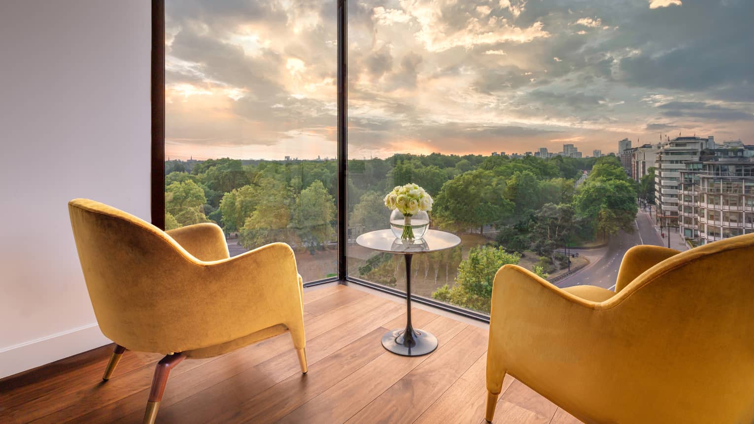 Two mustard-coloured club chairs and small round table on wood floor with views from large window