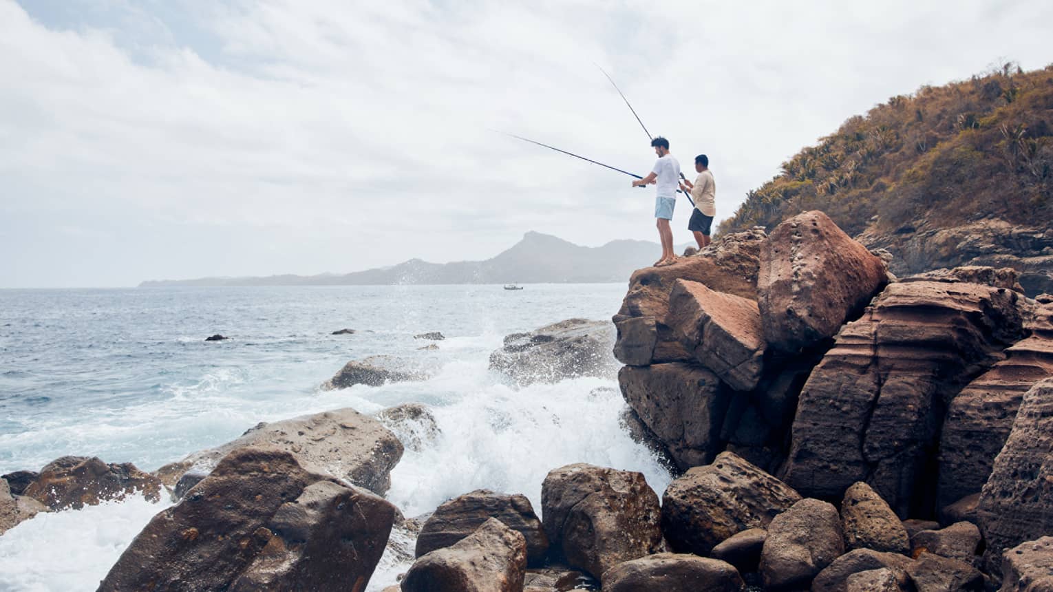 Two men on large rocks fishing in the ocean.