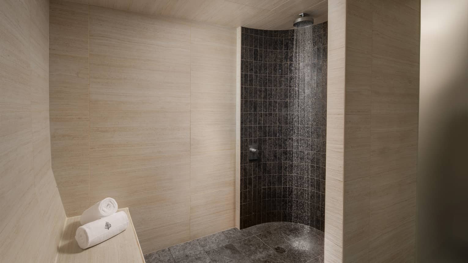 Tiled corner shower with rainfall fixture, white towels with Four Seasons logo on bench nearby
