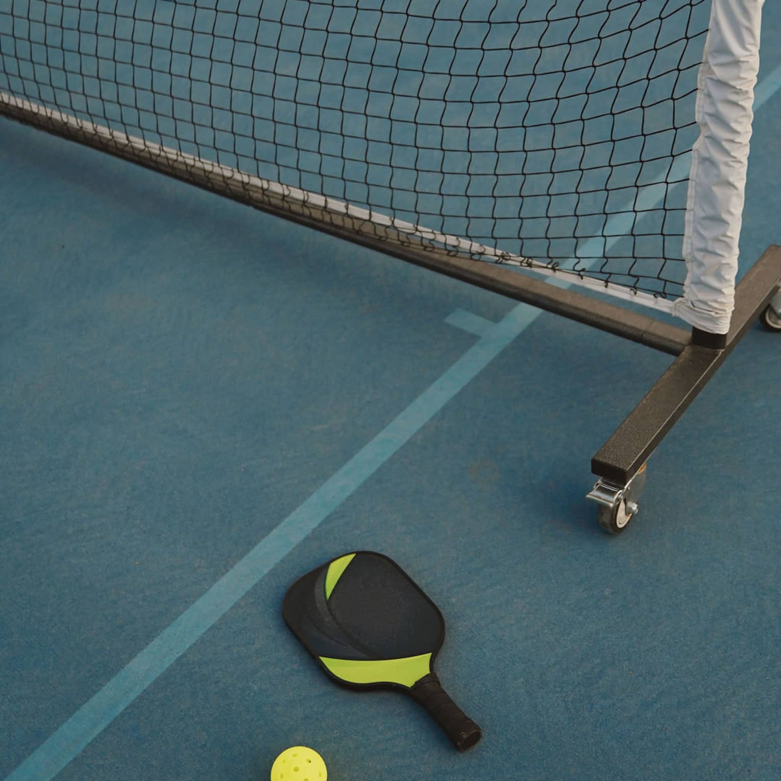 A pickleball paddle and ball on a pickleball court near the net