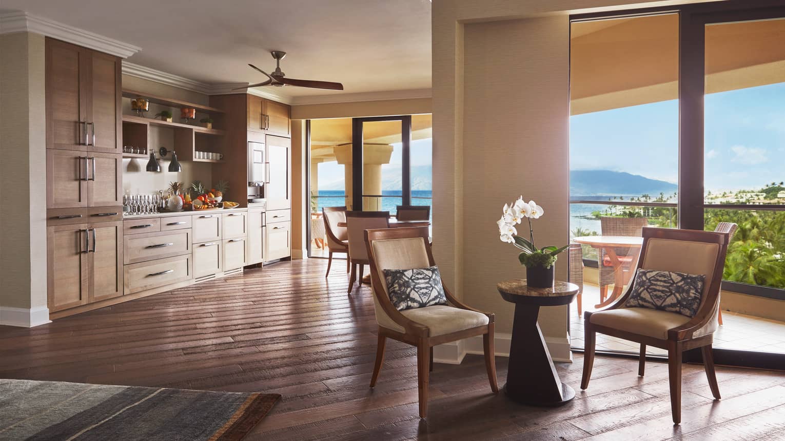 Open-concept suite with kitchenette, seating area and ocean-view balcony under natural light