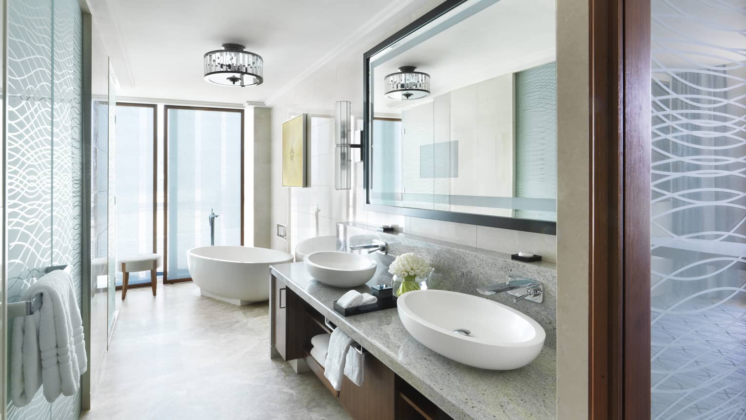 Modern bathroom with a freestanding bathtub, double sinks, a large mirror and frosted glass accents, filled with natural light