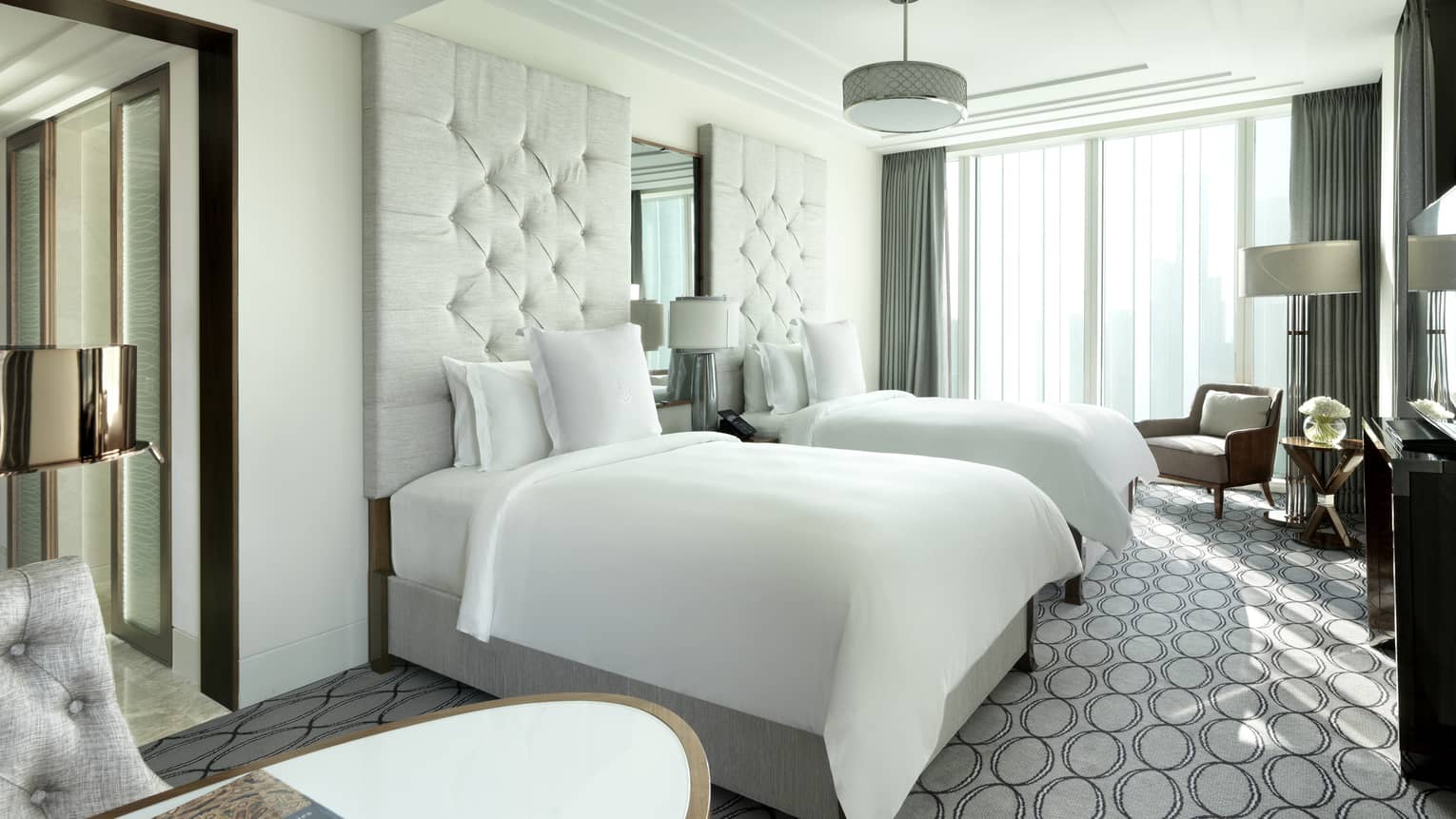 Bright hotel room with two plush twin beds, tufted headboards, modern decor and large windows letting in natural light