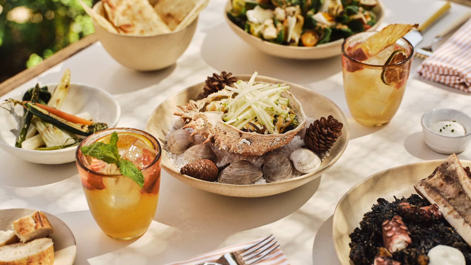 A variety of Spanish dishes set on a white-cloth table with two cocktails