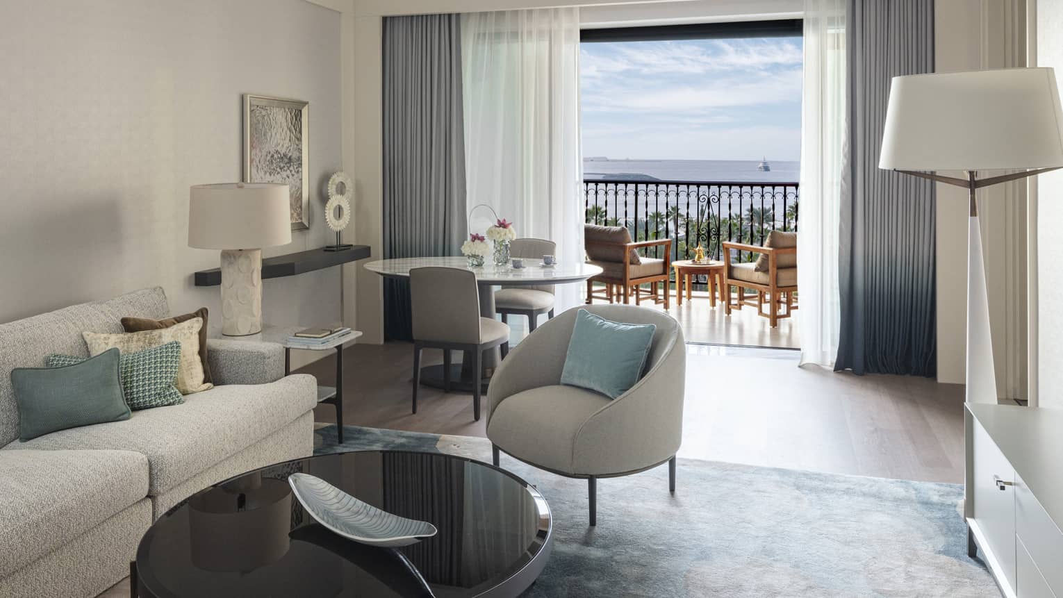 Living room of a hotel suite, with a sofa, arm chair, round table and two chairs, and a walk-out balcony