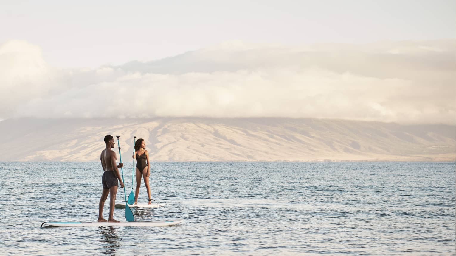 Man and woman stand on SUP paddleboards in the ocean in Maui