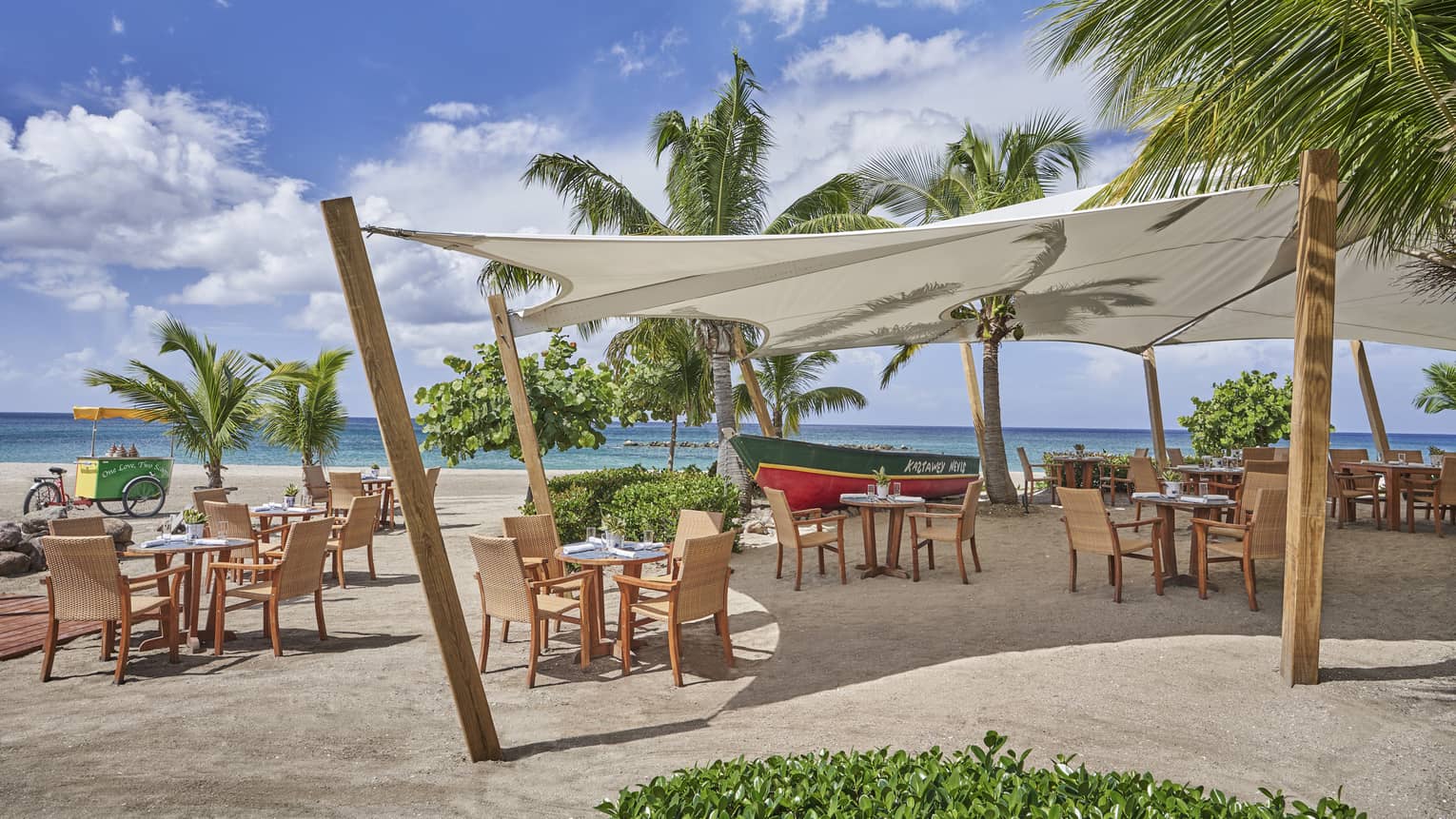 Cabana with beige chairs and tables on the beach with palm trees.