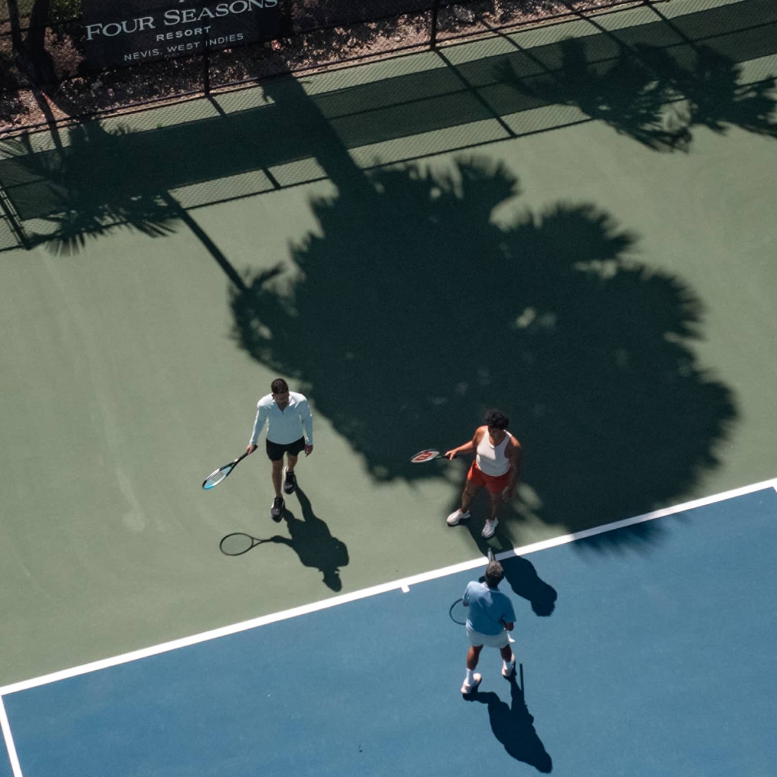 Three people holding tennis racquets on a tennis court.
