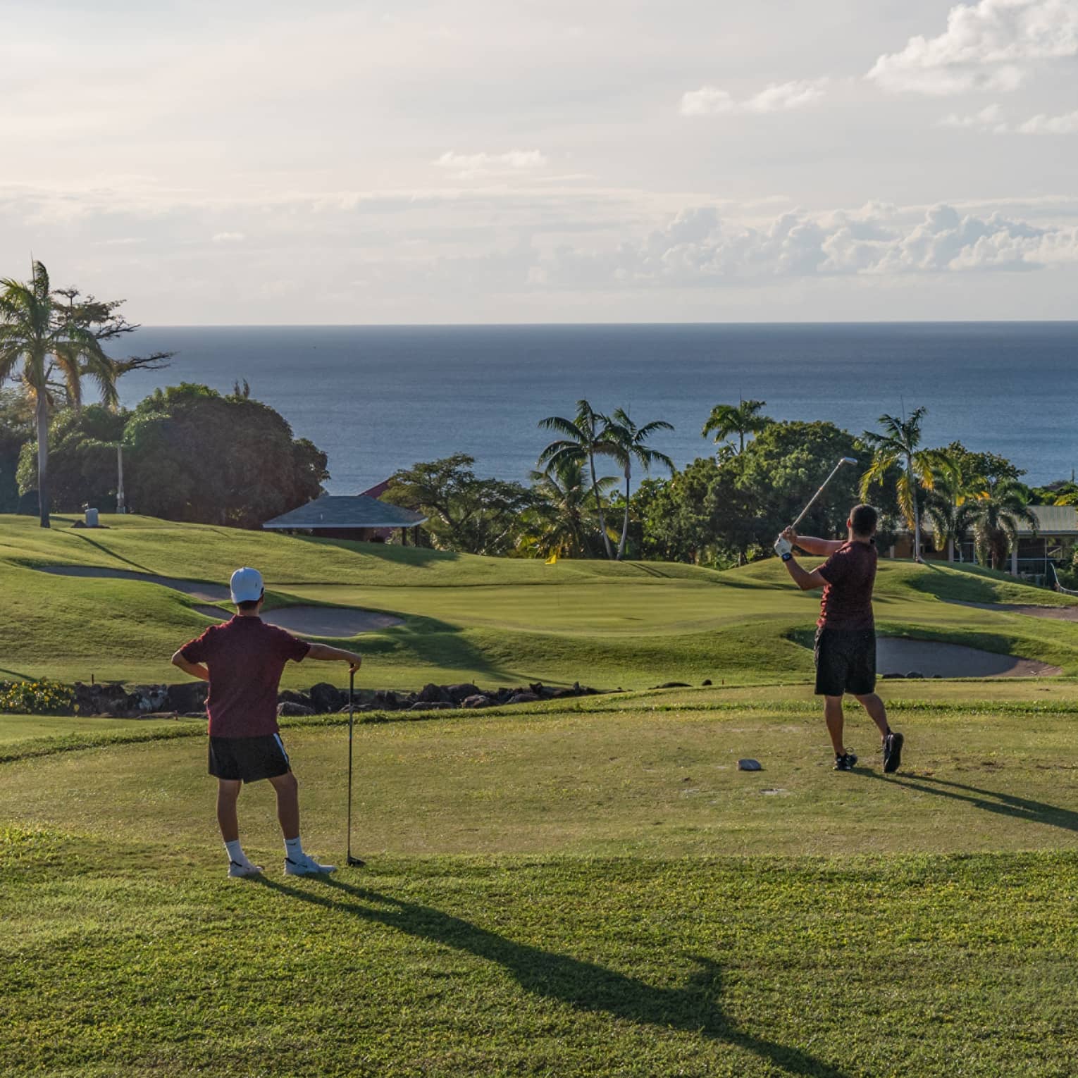 Two guests on a golf course near the ocean swinging golf clubs