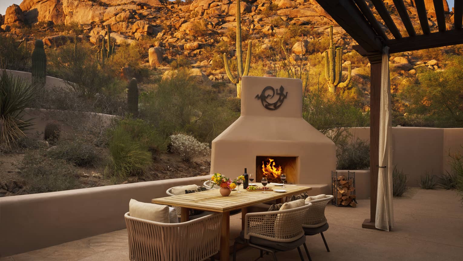 Private terrace of a resort suite, featuring a contemporary dining table, outdoor fireplace and views of the desert and rocky mountain