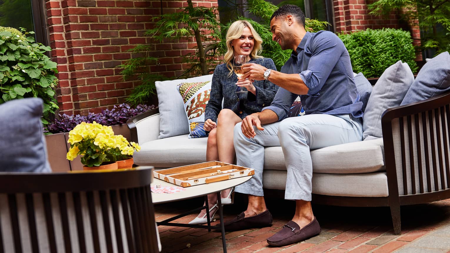 Two guests sitting on a couch at an outdoor patio and holding wine glasses