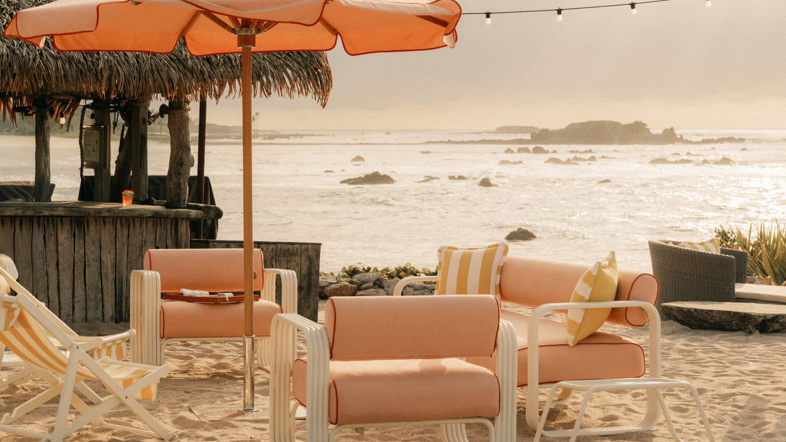 Light orange upholstered and fabric lounge chairs and sun umbrella on a beach with ocean and coastal views in the background