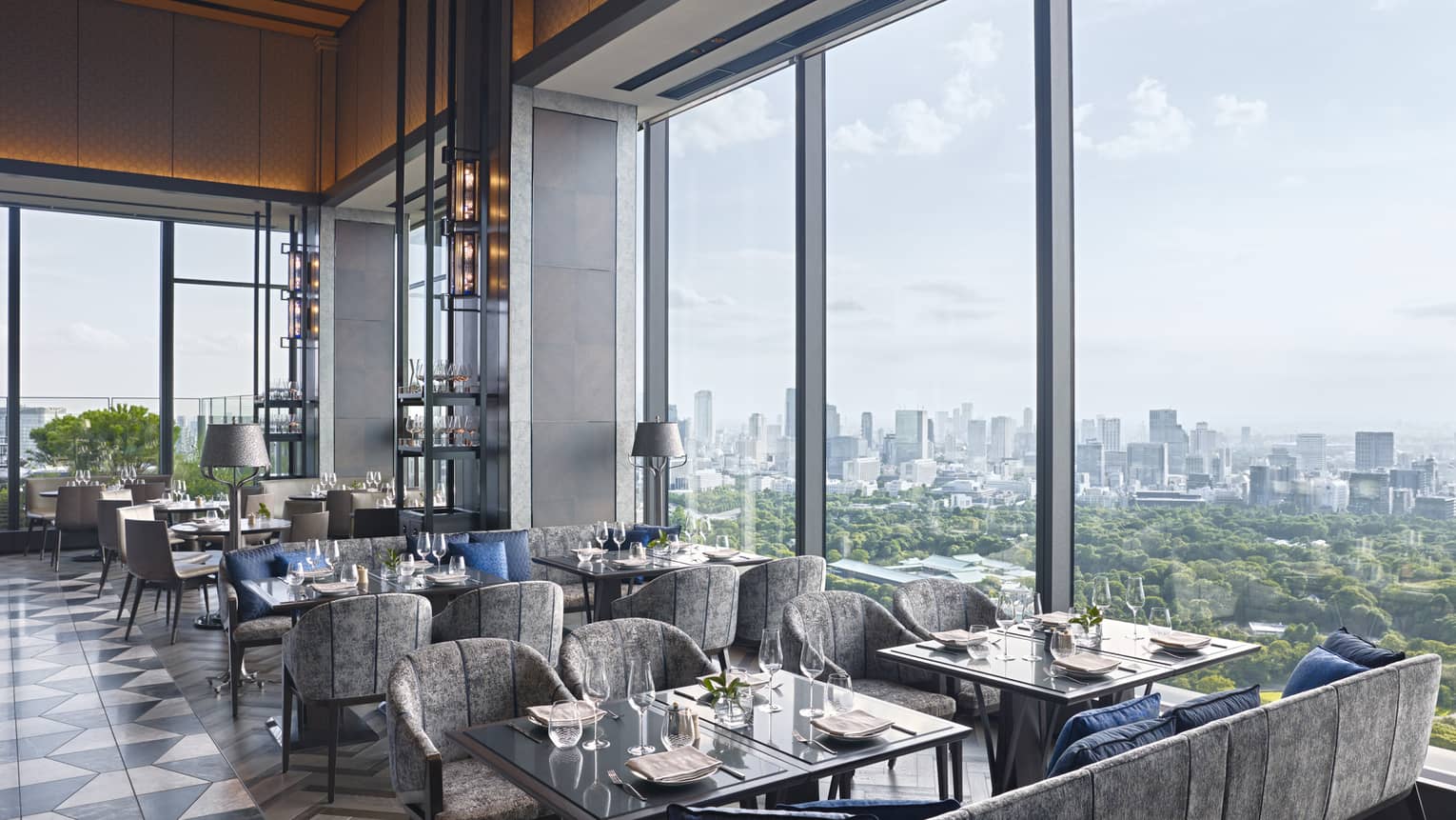 Restaurant with square tables and grey chairs/sofas, black-and-white tile floor, wall of windows looking out to Imperial Gardens in Tokyo