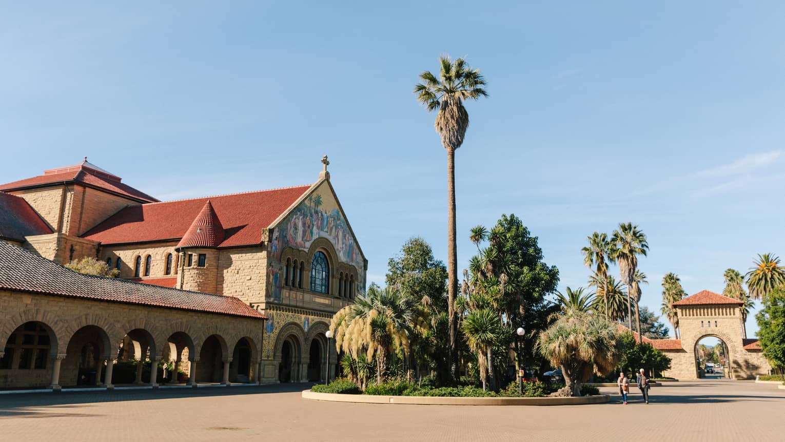 Palm trees next to a large brown and red building on a sunny day.