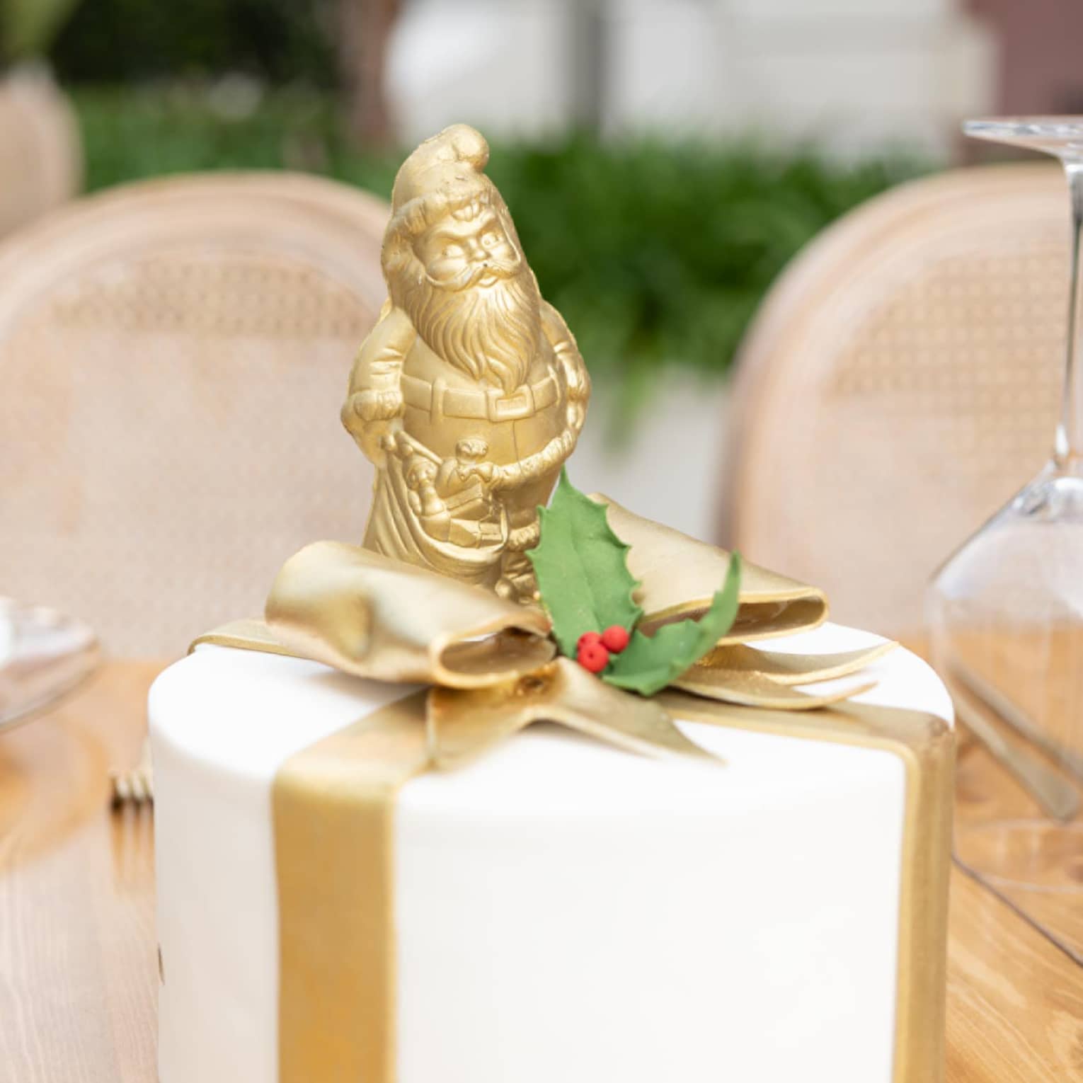Round white cake decorated with gold fondant bow and a golden Santa Claus on top
