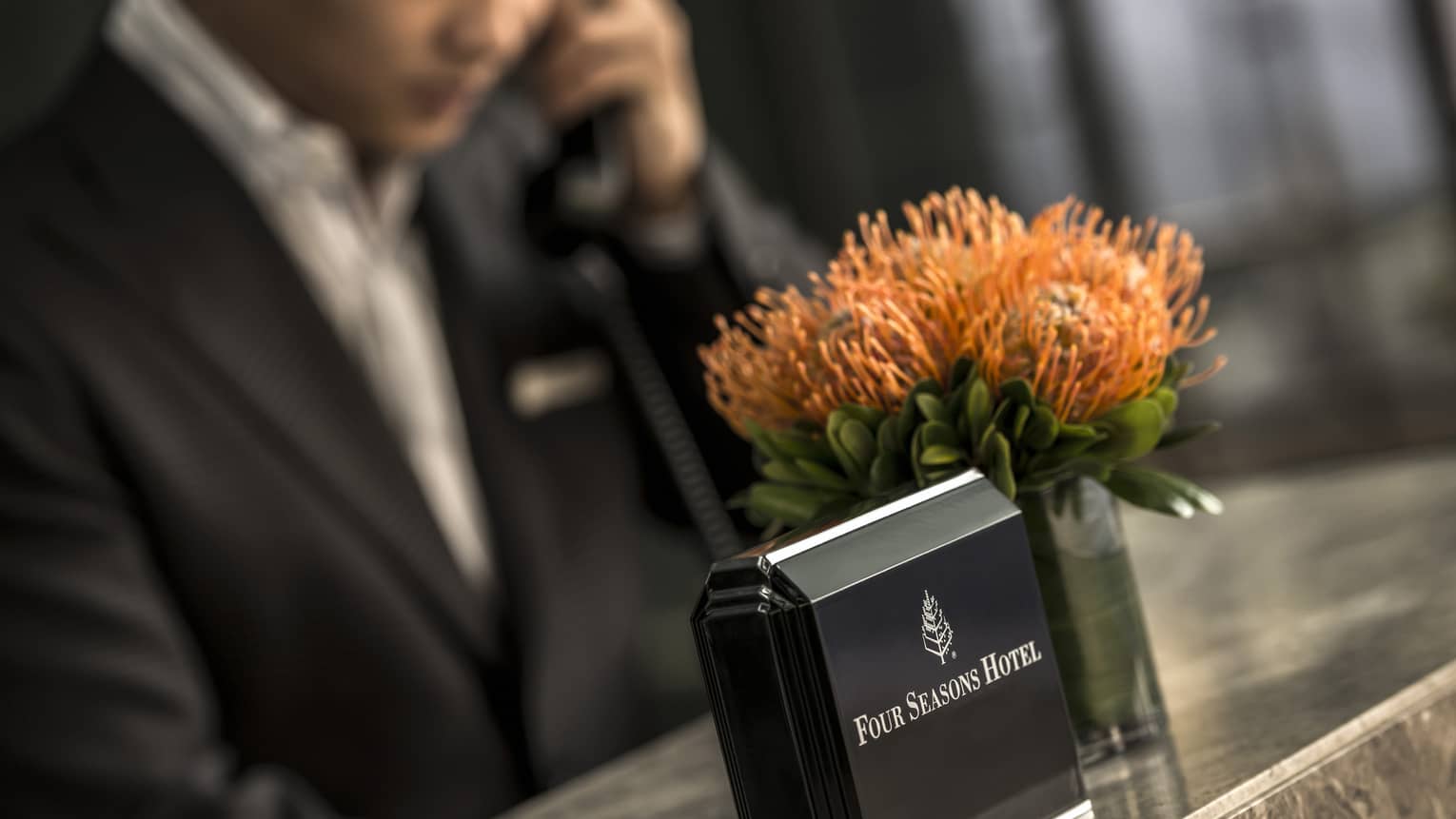 Close-up of Four Seasons Hotel concierge desk, orange flowers in vase, staff on phone