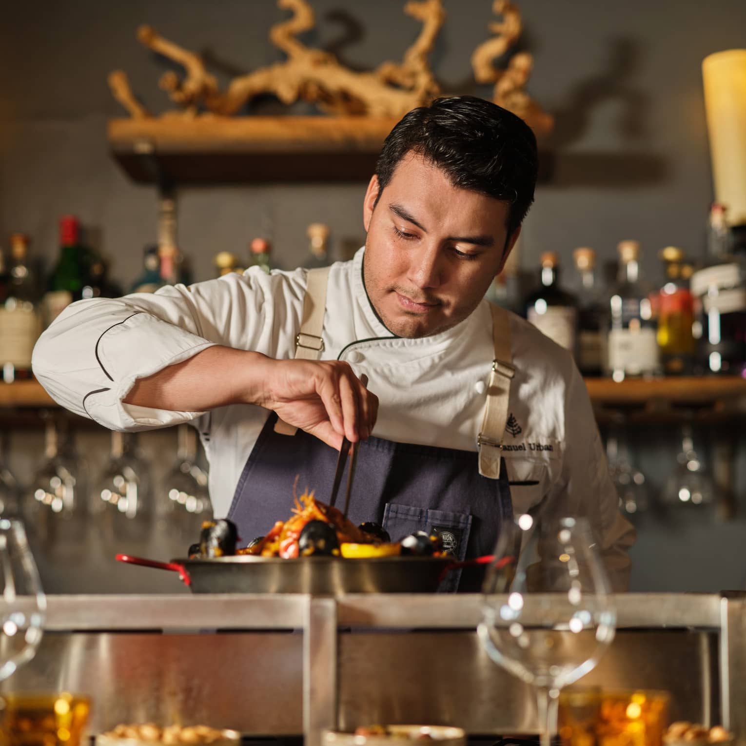 Chef wearing an apron and cooking a dish in a pan.
