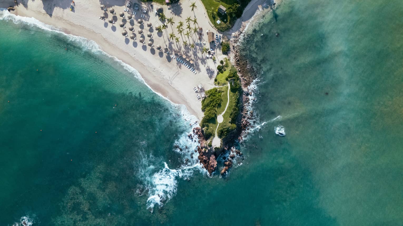 A bird's-eye view of a point of land with a beach, surrounded by blue-green ocean