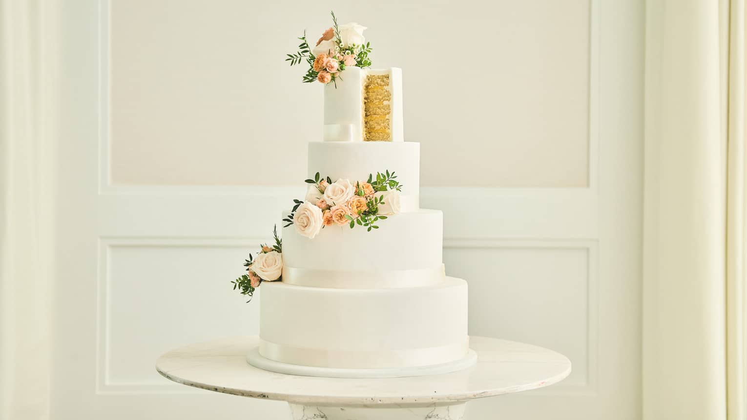 White four-tier wedding cake with peach and white flower spray cascading down its side