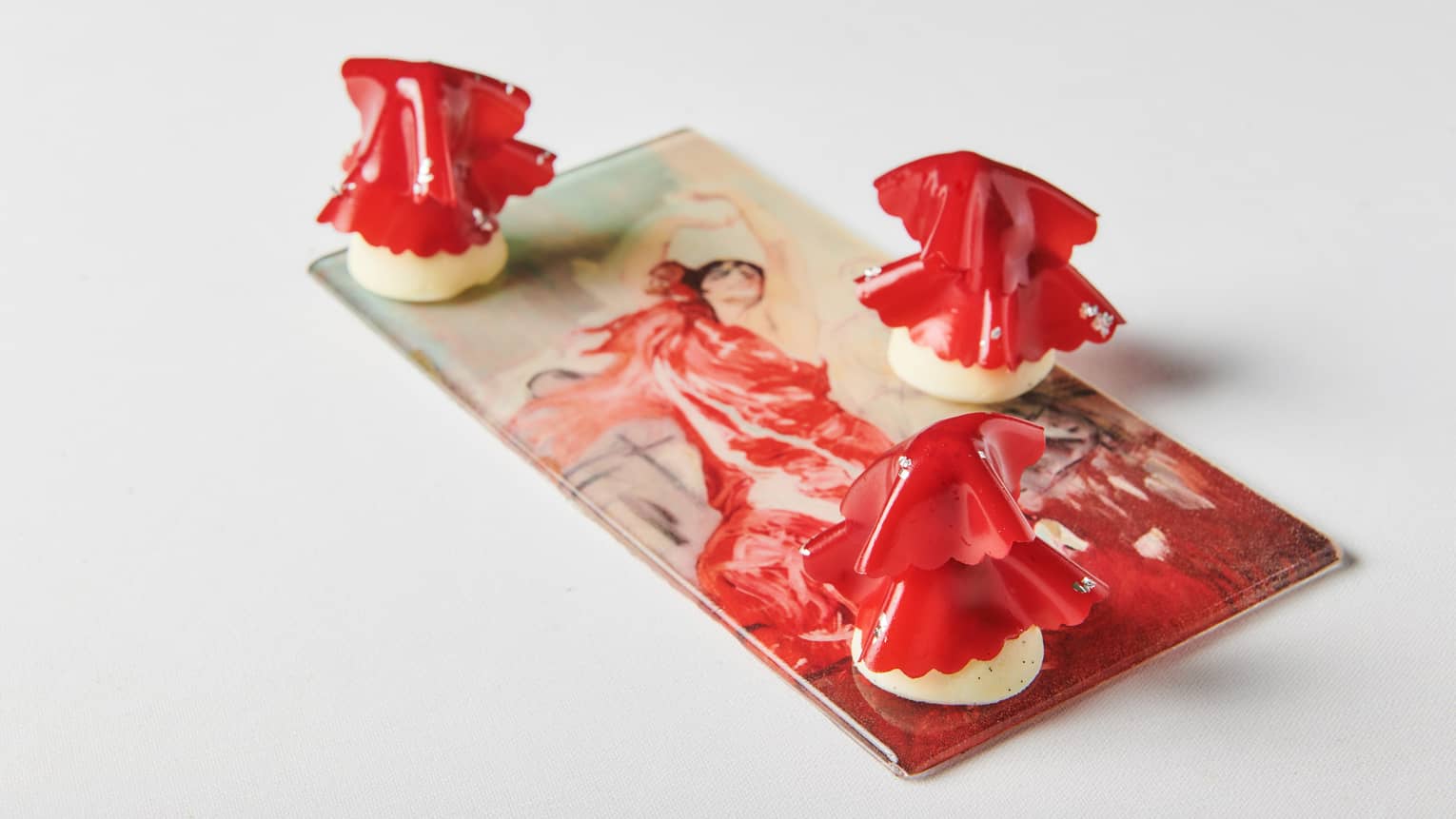 Three bright-red pastries arranged on a painted tile of a woman in a red dress