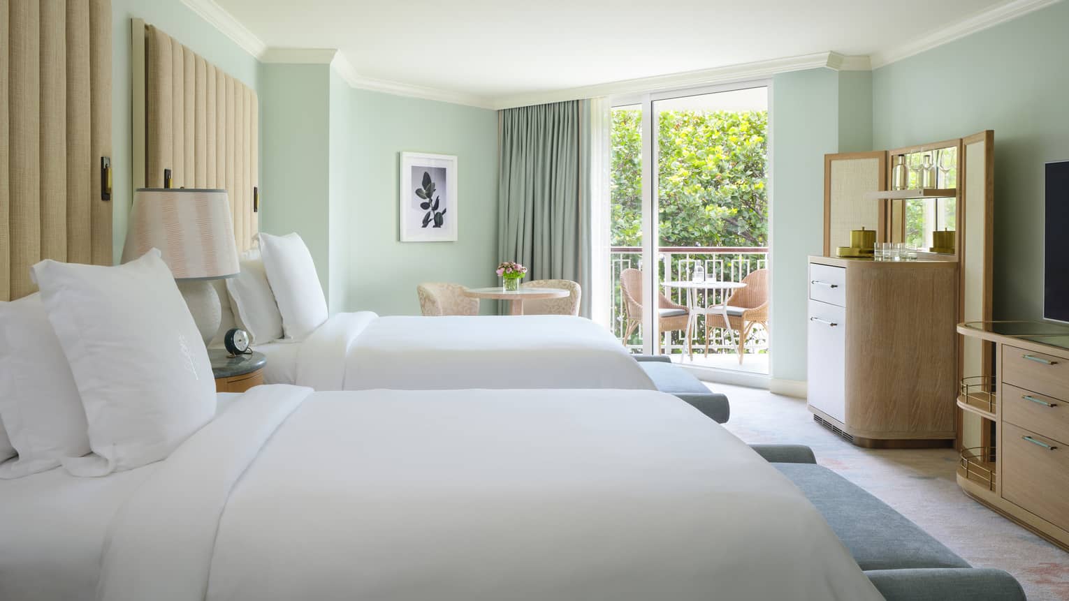 Luxury resort guest room with two beds, light green walls, cream upholstered headboards and balcony at Four Seasons Resort Palm Beach