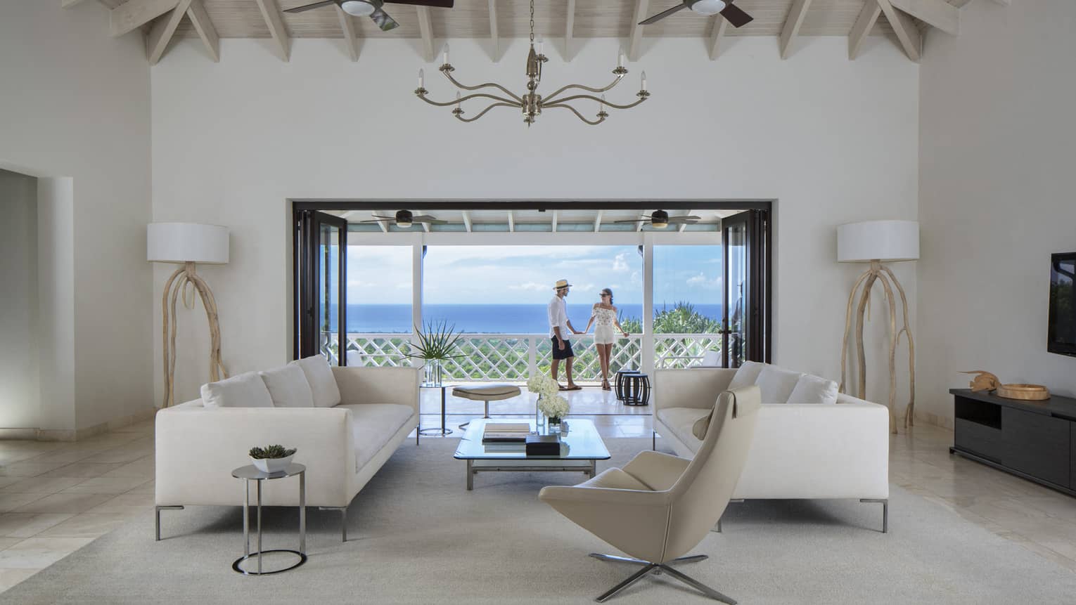Living room with modern white furniture in front of open doors to sunny patio, couple