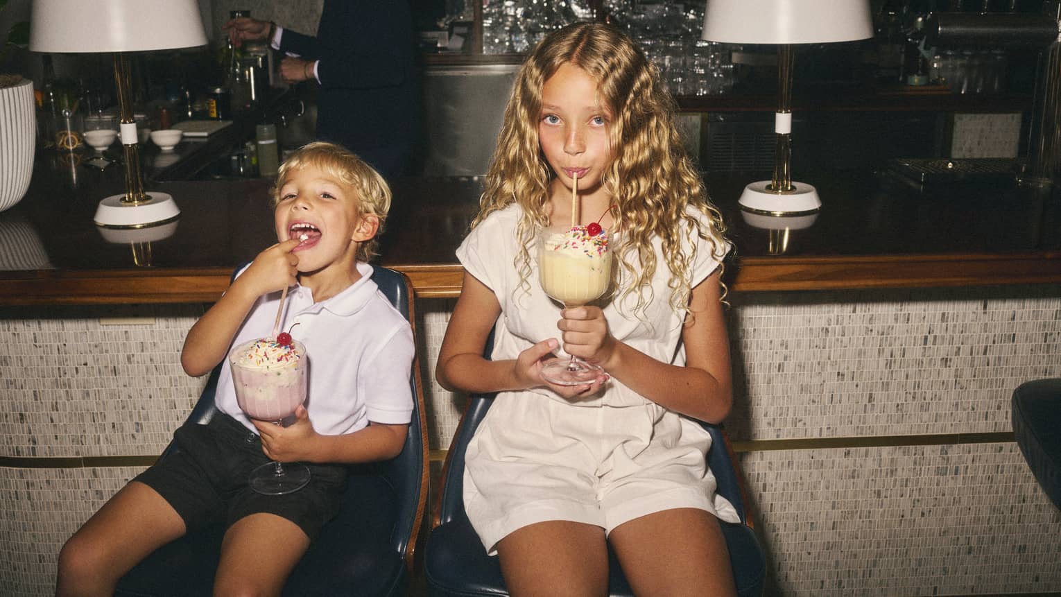Two children sit on counter stools sipping on large milkshakes