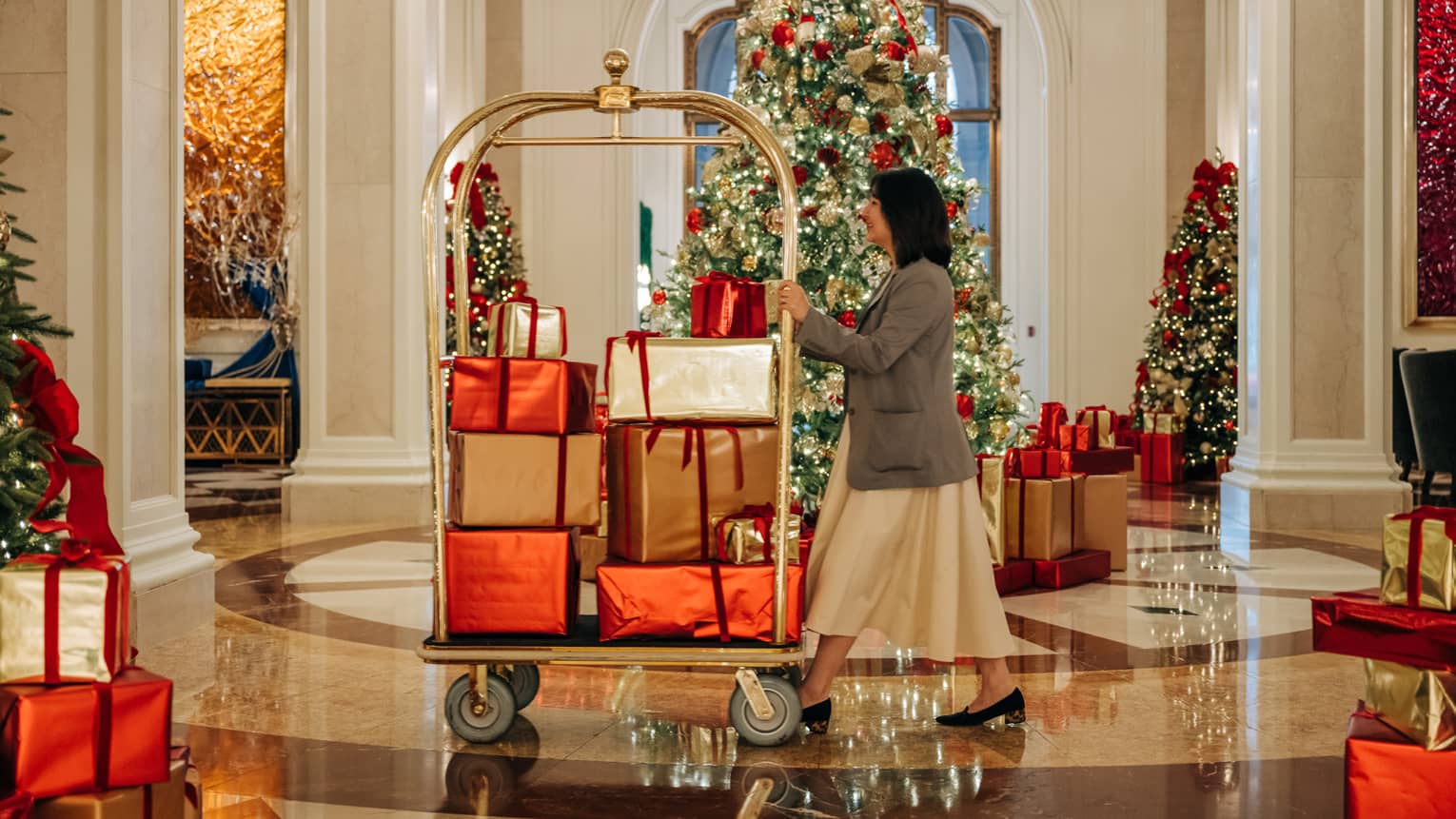 Hotel staff member rolls a luggage cart filled with presents through a lobby decorated for Christmas
