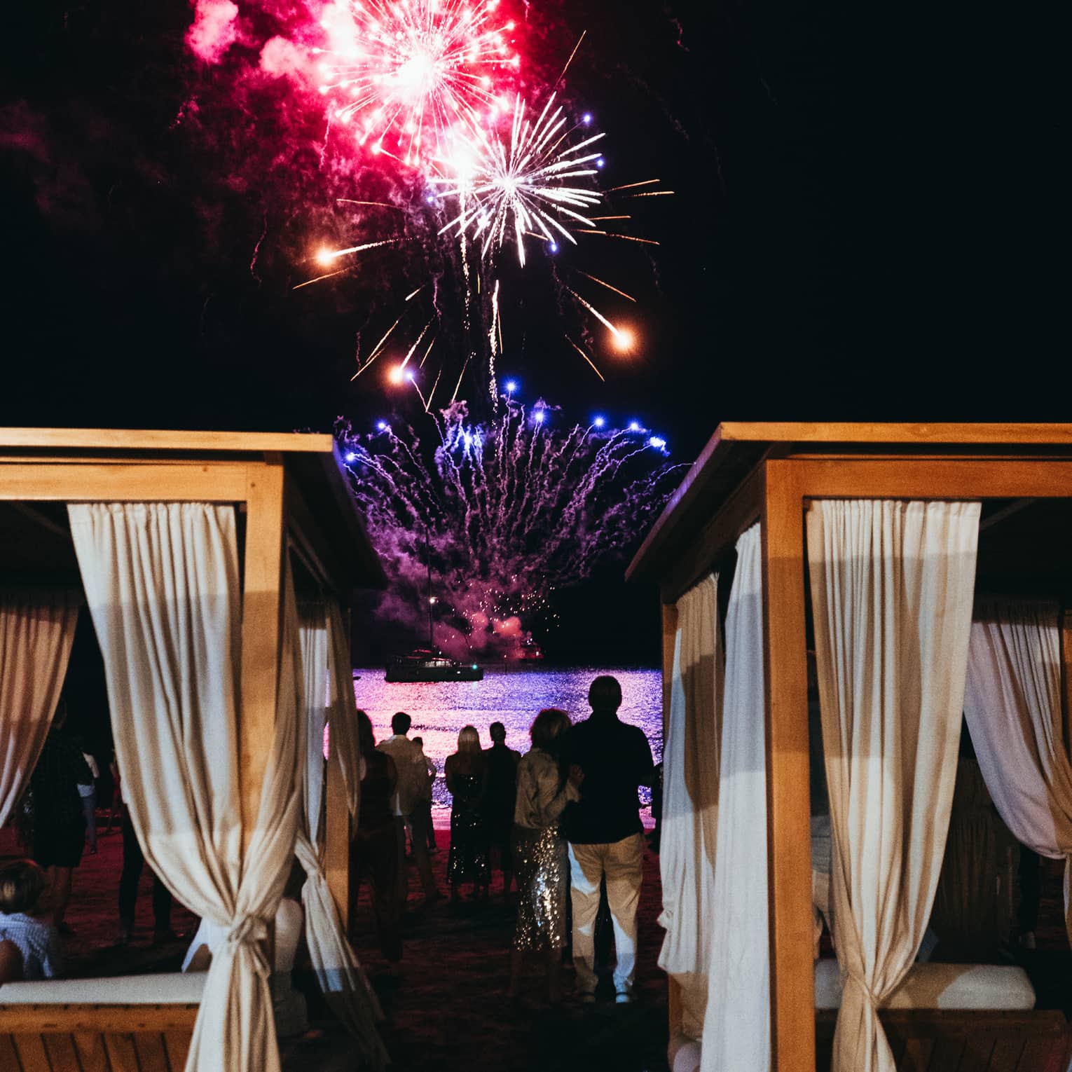 Fireworks light up the night sky over rows of beach cabanas