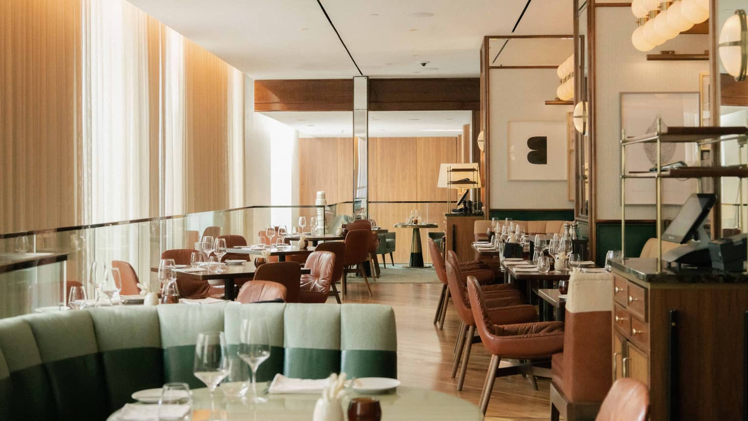 The interior of a softly lit restaurant with floor-to-ceiling curtains on one side of the room.