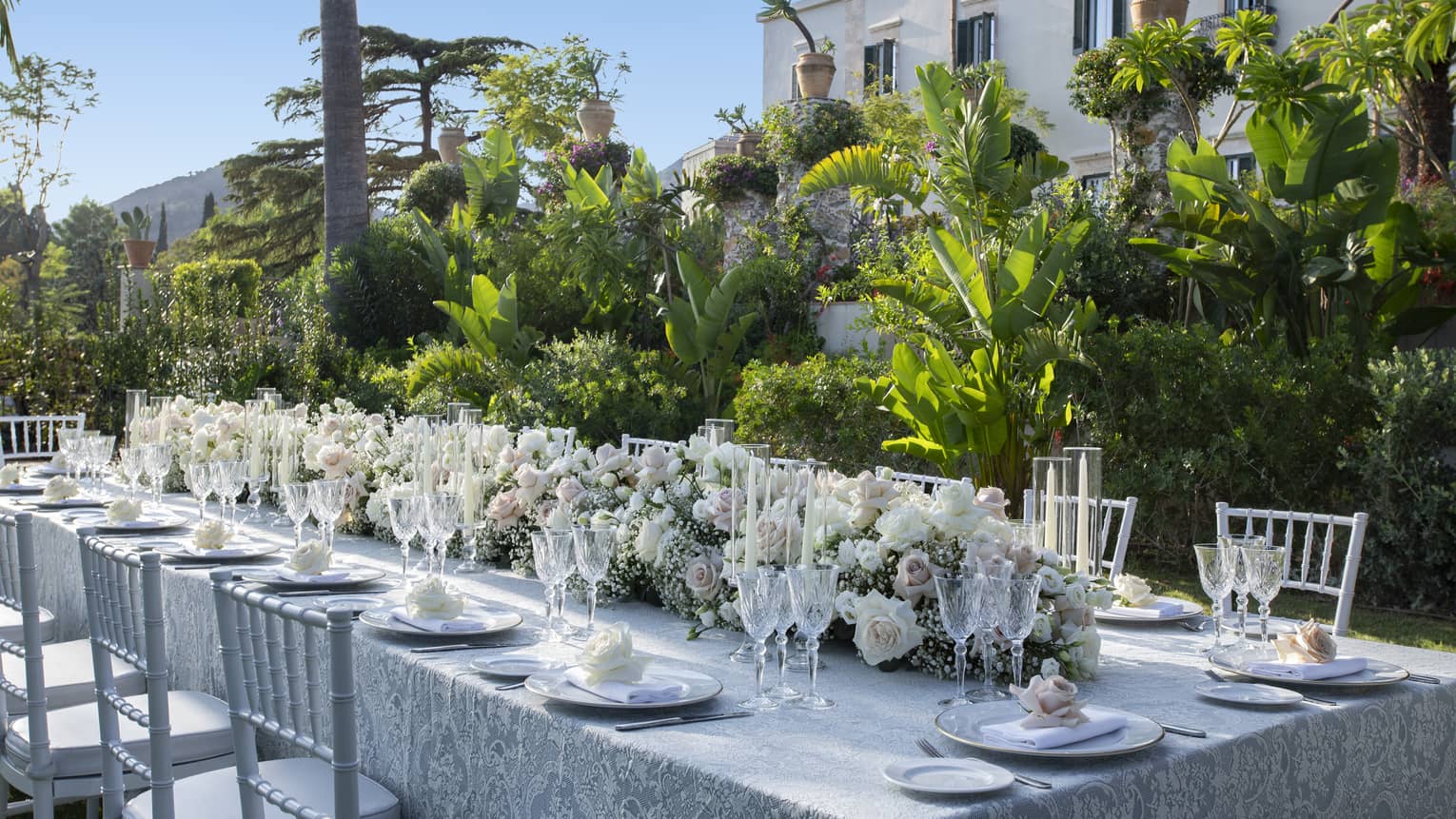 Elegantly set long table with extended floral wedding centrepiece alongside lush garden wall