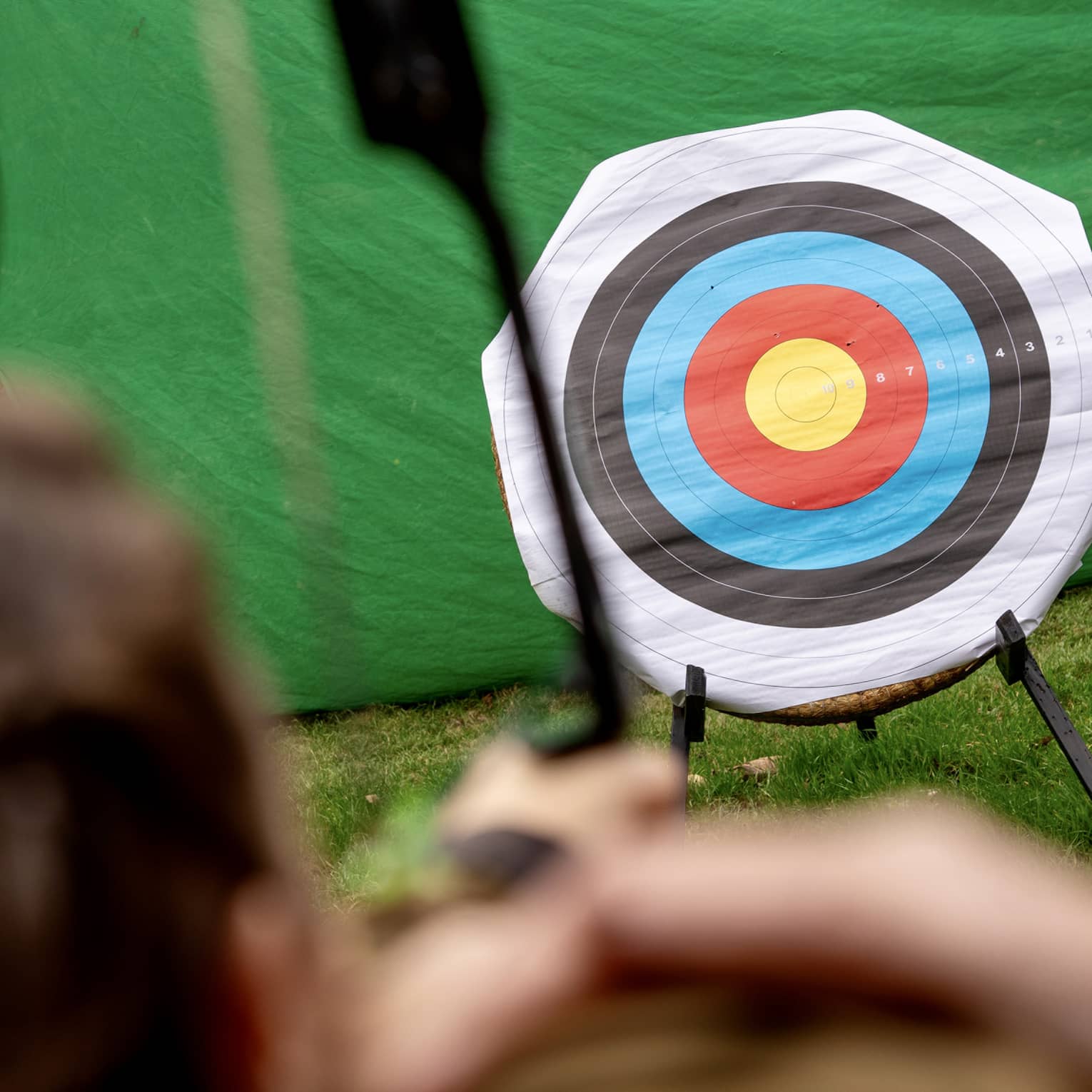 Rear view of an arbalist aiming their crossbow at a bull's-eye of yellow, red, blue, black and white concentric circles.