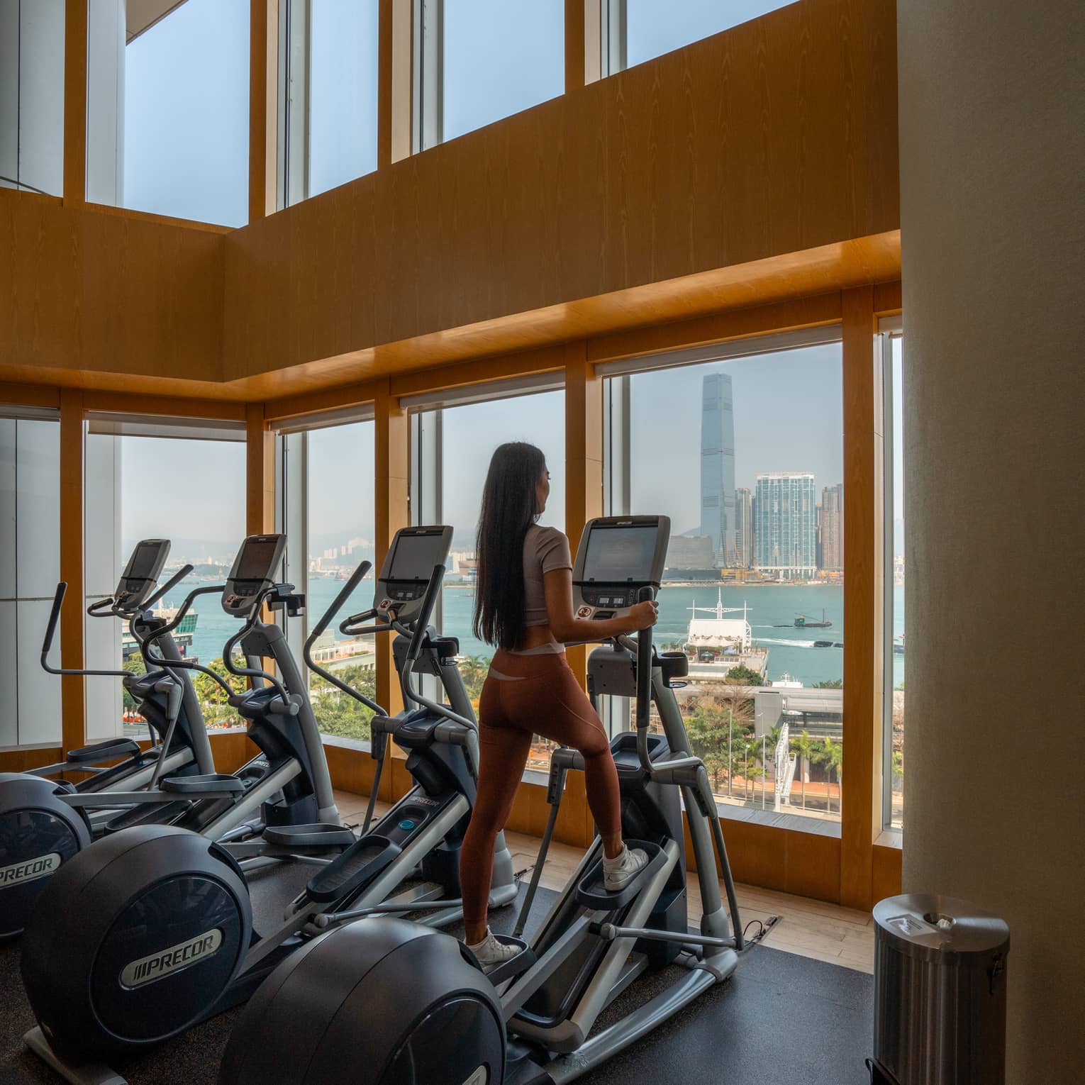 Woman is on elliptical facing city view window at fitness centre at Four Seasons Hotel Hong Kong