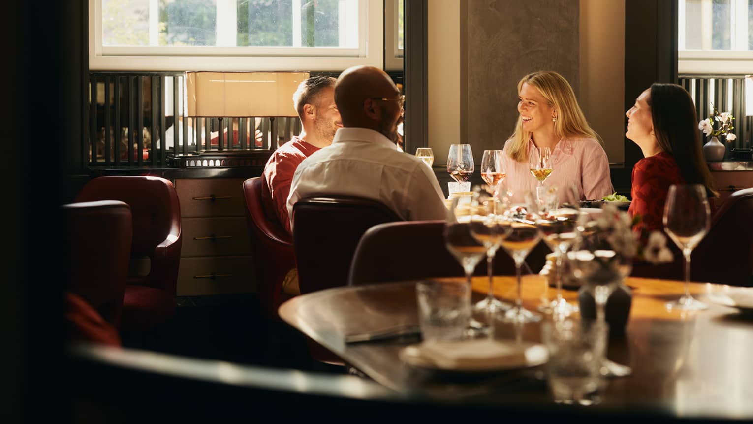 People sitting around a table, enjoying a meal in an indoor dining space. The table is next to a window that is letting in bright natural light.