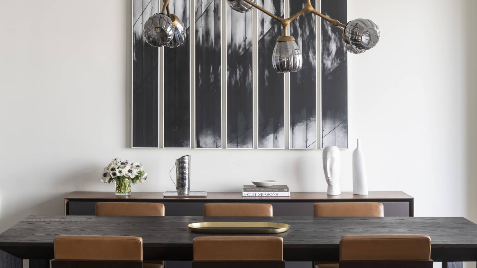 Abstract black and white paining on white wall next to six-seat dining table, contemporary hanging lamp