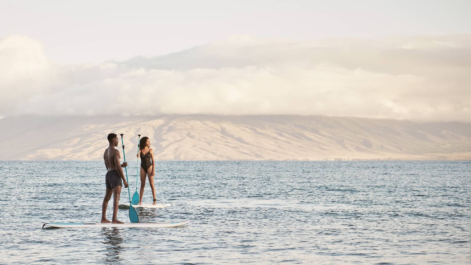 Man and woman stand on SUP paddleboards in the ocean in Maui