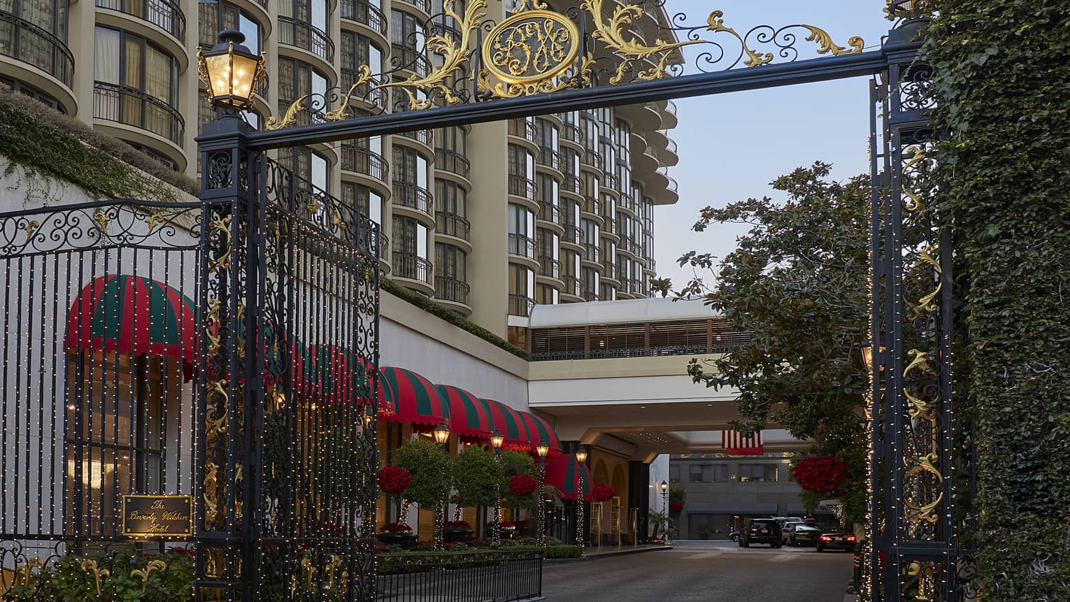 A metal gate with gold decoration at the entrance to a long driveway next to a hotel.