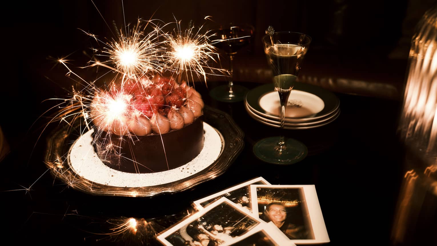 Sparkler candles in a chocolate cake and polaroid pictures nearby on a table