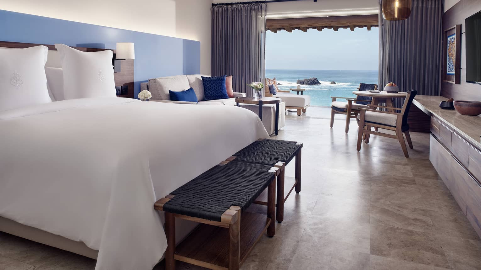 A hotel room with a bed, large window, chairs, and a sofa.