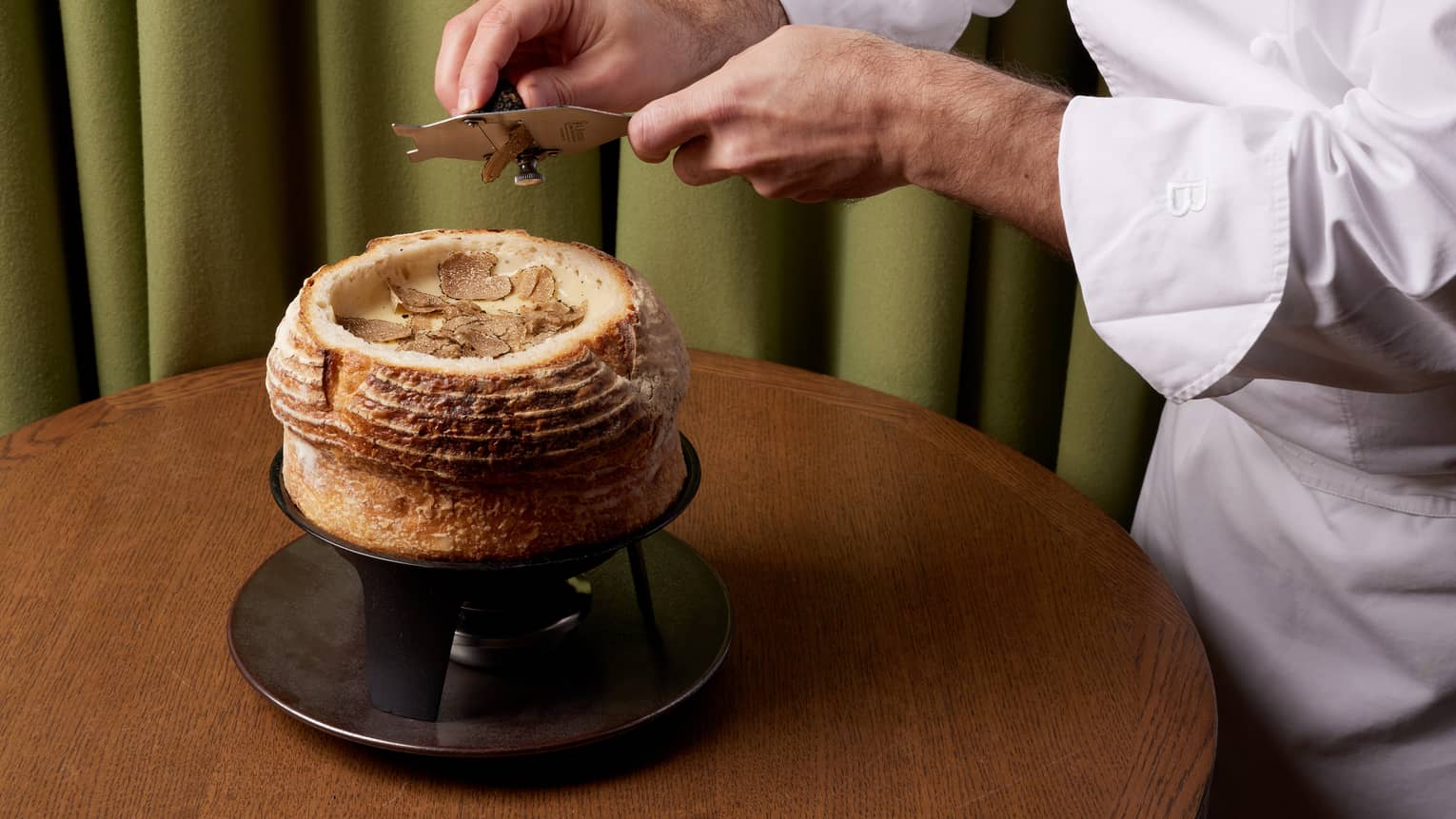 Chef in white chef's coat shaving truffle atop cheese fondue in bread bowl