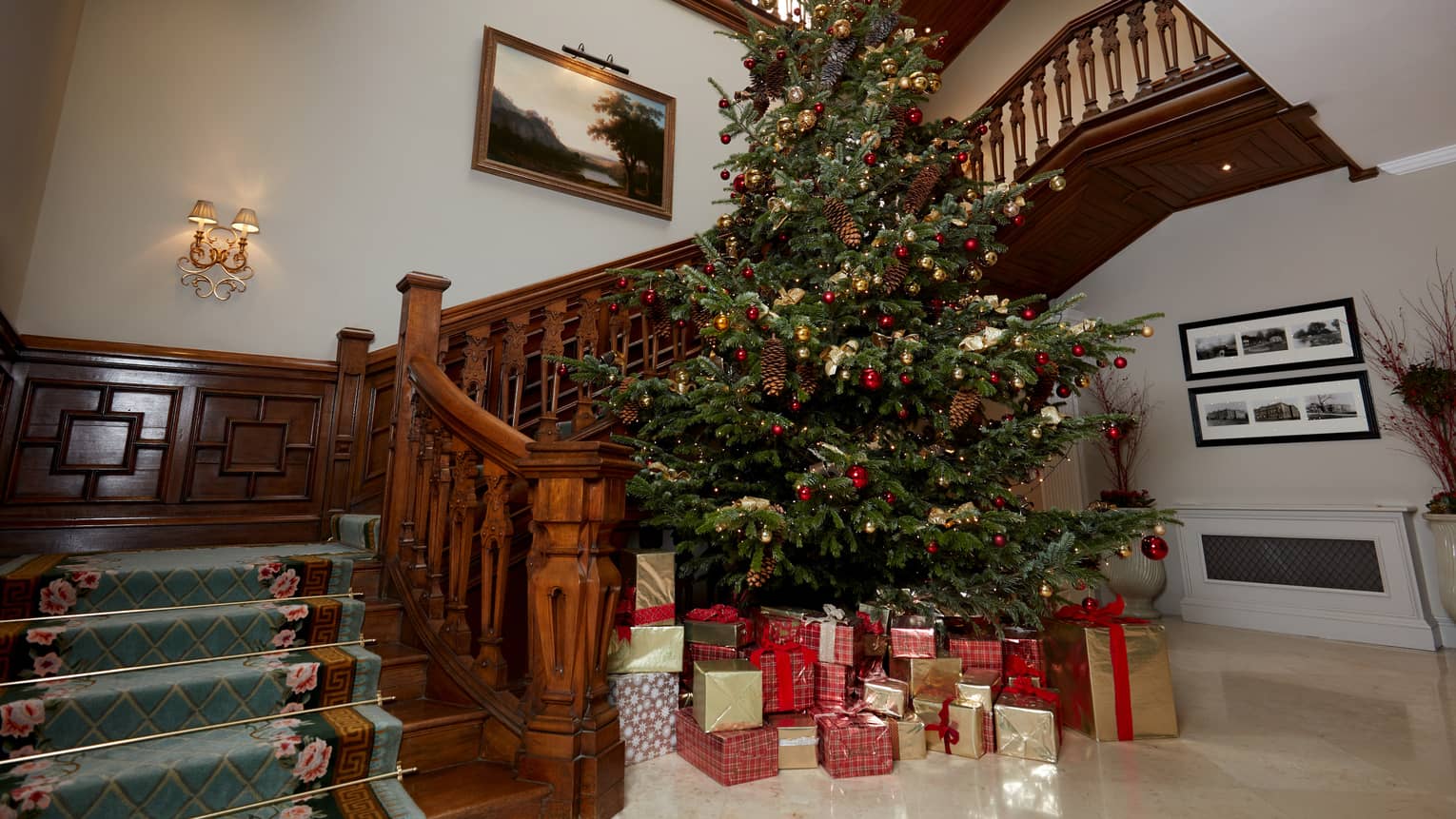 Curved carved wooden staircase with tall Christmas tree beside it laden with wrapped gifts