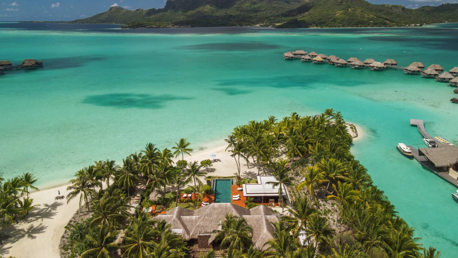 Aerial view of Bora Bora villa on edge of turquoise lagoon, looking out to overwater bungalows and mountains
