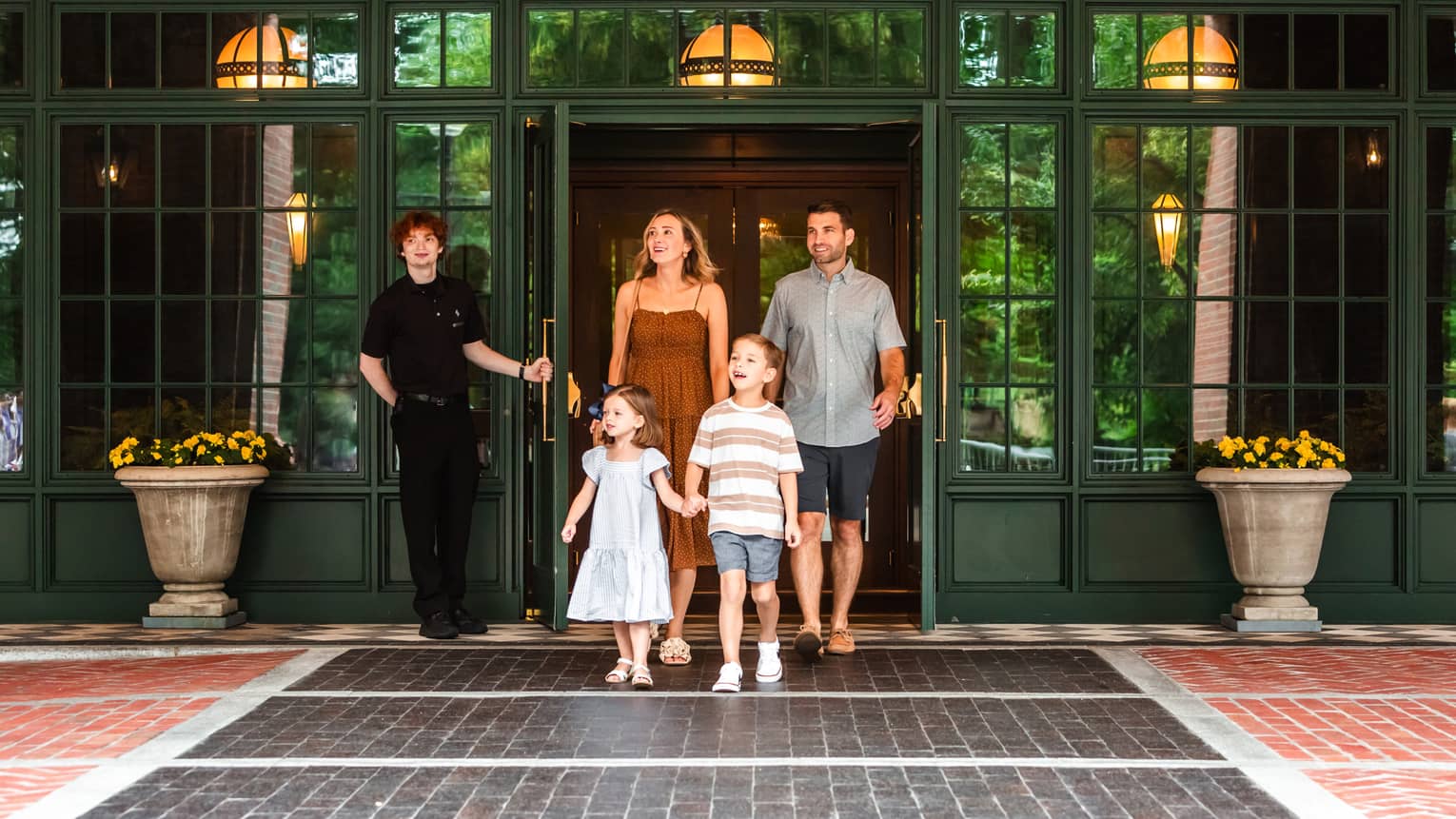 A person holding the door for four guests leaving a green building