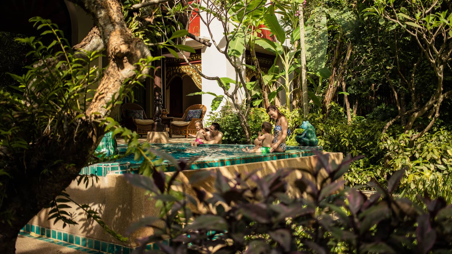 Family relaxing in a private plunge pool surrounded by tropical plants and traditional architectural details.