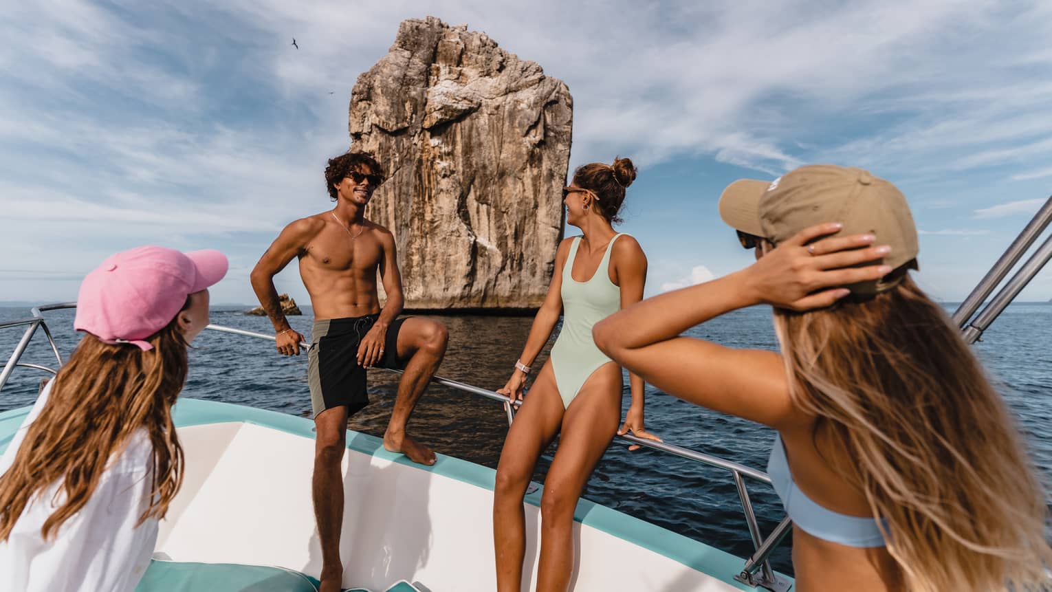 Four guests wearing colourful swimsuits ride in a boat toward a rocky outcropping in the ocean