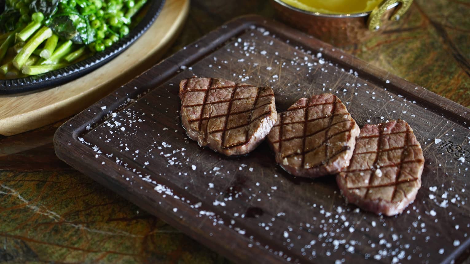 Grilled steaks served on a wooden board and garnished with course salt