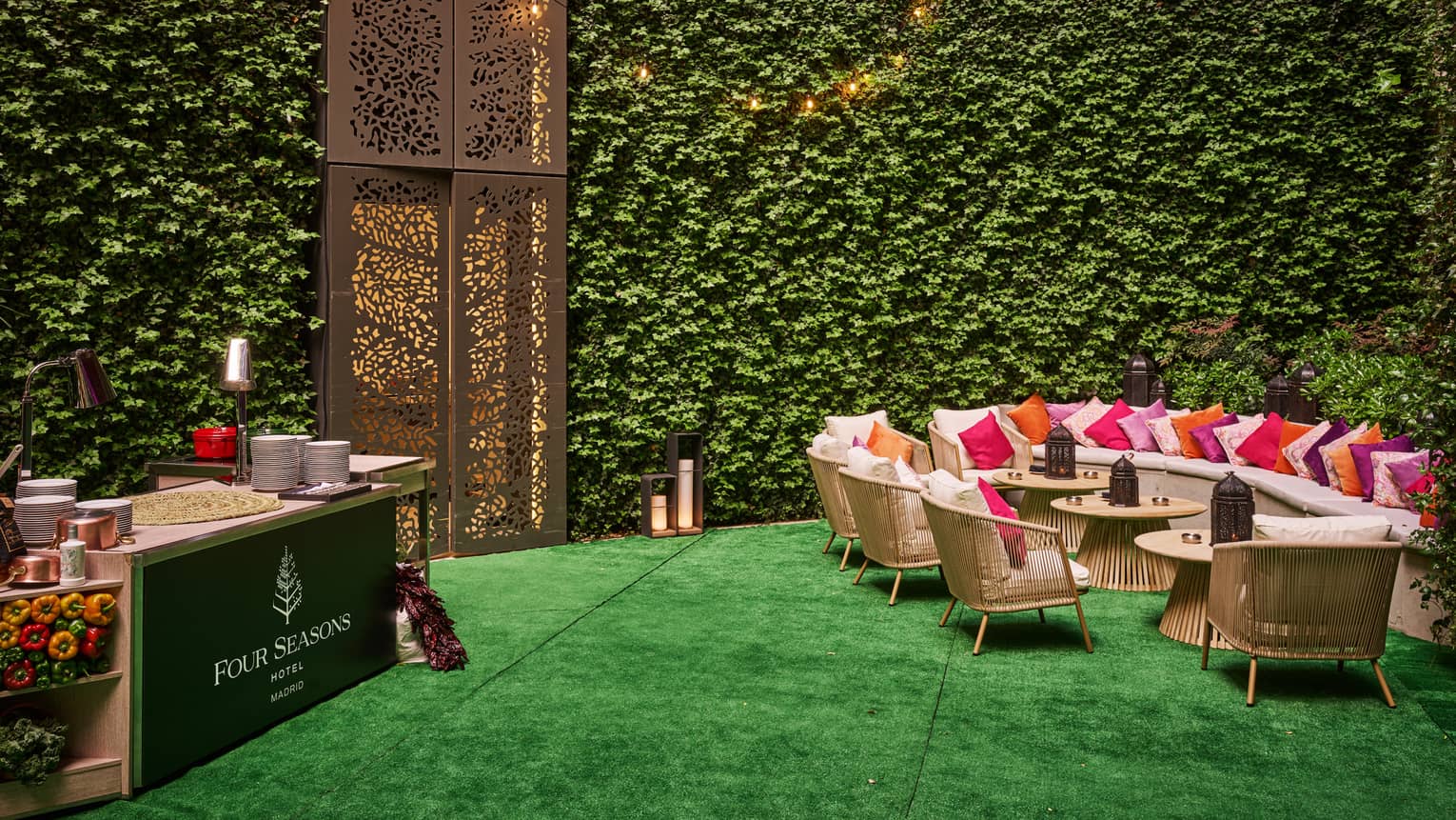 Courtyard with green tuf flooring, vine-covered walls, long cream sofa, three rattan coffee tables and four rattan arm chairs