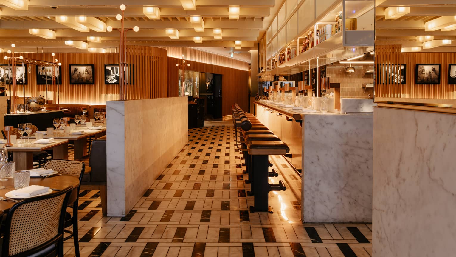 Interior of a restaurant dining room with black-and-white tiled floors, marble coutners and a chef's counter