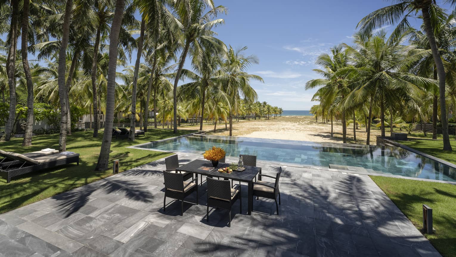 Three-Bedroom Pool Villa pool area with dining table, lounge chairs, palm trees, ocean views