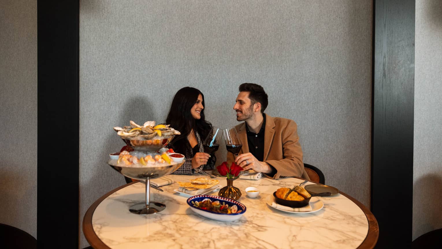 Man and woman sitting at table and clinking wine glasses.